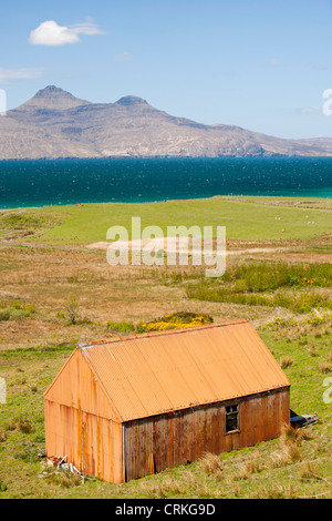 Eine alte Wellblech-Scheune am Cleadale auf der Insel Eigg, mit Blick auf die Isle of Rum, Schottland, UK. Stockfoto