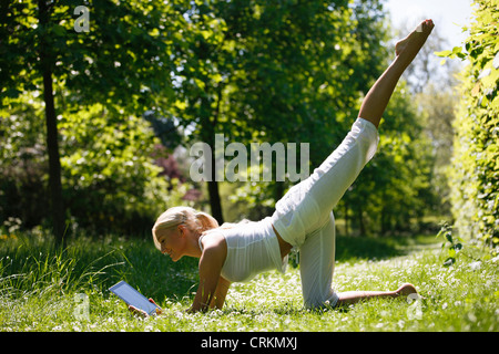 Eine junge Frau, die mit Blick auf eine digital-Tablette während Yoga außerhalb üben Stockfoto