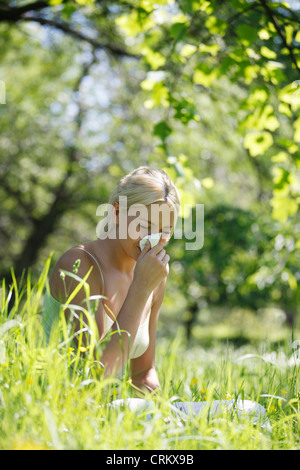 Eine junge blonde Frau in ein Papiertaschentuch Niesen Stockfoto