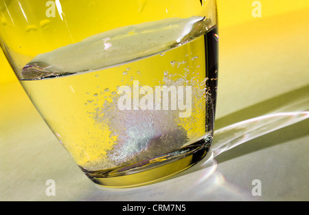 Tablette auflösen in einem Glas water.against einen gelben Hintergrund. Stockfoto