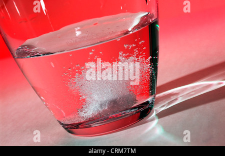 Tablette, übervoll, wie es in ein Glas Wasser vor einem roten Hintergrund auflöst. Stockfoto