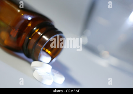 Weiße Paracetemol Tabletten aus einer braunen Flasche in der Nähe von einem Glas Wasser. Stockfoto