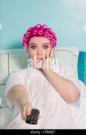 Porträt von schockiert Frau hält remote mit Lockenwicklern sitzt auf Bett Stockfoto