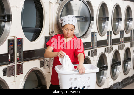 Junge weibliche Angestellte mit Wäschekorb mit Waschmaschinen im Hintergrund Stockfoto