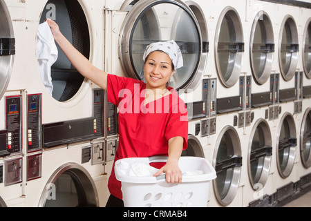 Porträt der glückliche junge Arbeitnehmerin putting Kleidung in der Waschmaschine Stockfoto