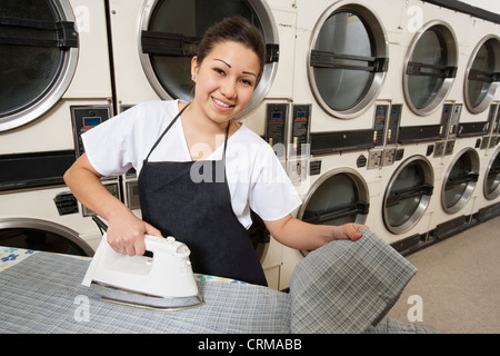 Porträt einer glücklichen Frau mit Schürze Bügeln vor Waschmaschinen Stockfoto