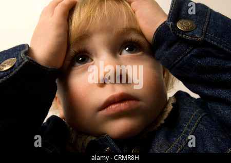 Kleiner Junge hielt seinen Kopf mit seinen Händen Stockfoto