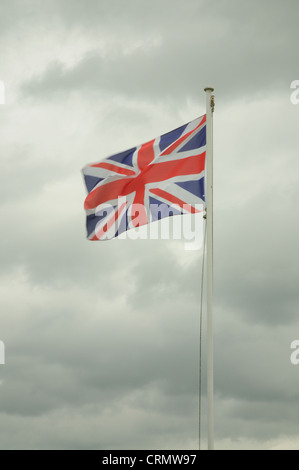 Union Jack-Flagge des Vereinigten Königreichs auf eine Fahnenstange im Wind mit einem stark bewölkt und düsteren Himmel Stockfoto