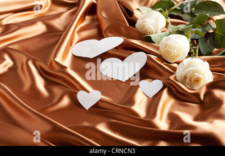 Blumen und Papierherzen auf einem goldenen Satin. Weihnachtskarten Stockfoto