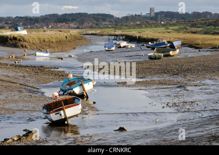 Kleine Boote vor Anker in Morston Creek bei Ebbe mit Blakeney Dorf und Kirche in der Ferne. Stockfoto