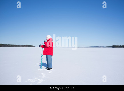 Ältere Kakausenfrau bohrt mit dem Handeis-Augur am See Niinivesi, Finnland, ein Loch nach Eis Stockfoto