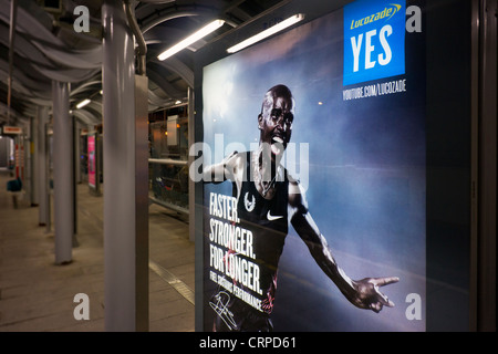 Werbung Board auf einer Plattform der Docklands Light Railway in der Nacht. Stockfoto