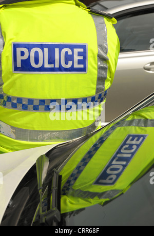 Ein Polizist Logo spiegelt sich in seinem Streifenwagen Windschutzscheibe. Gelbe Westen mit blauen Polizei-Logo. Stockfoto