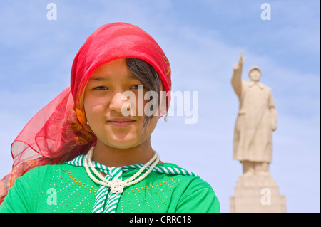 Eine junge Chinesin Uyghur posieren für die Kamera mit der Statue von Mao Zedong hinter in Kashgar. Stockfoto