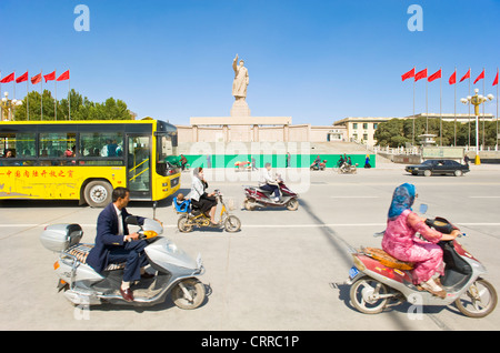 Mit Bewegungsunschärfe.  Fahrzeuge und Personen reisen Sie vorbei an der Statue von Mao Zedong gegenüber dem Stadtplatz in Kashgar. Stockfoto