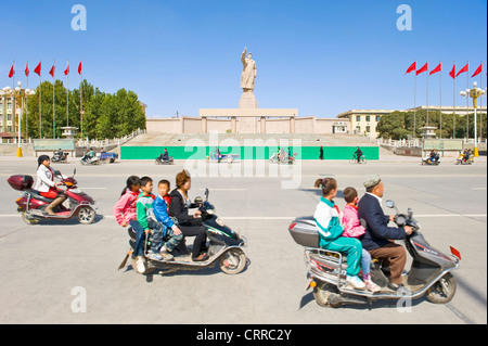 Mit Bewegungsunschärfe.  Fahrzeuge und Personen reisen Sie vorbei an der Statue von Mao Zedong gegenüber dem Stadtplatz in Kashgar. Stockfoto