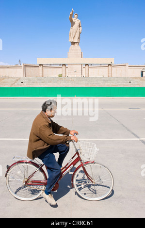 Mit Bewegungsunschärfe.  Ein chinesischer Mann auf dem Fahrrad fährt vorbei an der Statue von Mao Zedong in Kashgar. Stockfoto