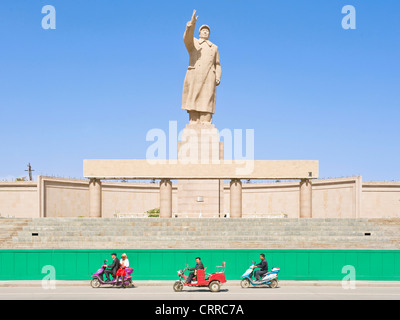 Mit Bewegungsunschärfe.  Fahrzeuge und Personen reisen Sie vorbei an der Statue von Mao Zedong gegenüber dem Stadtplatz in Kashgar. Stockfoto