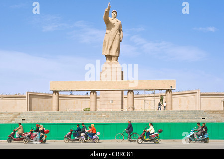 Mit Bewegungsunschärfe.  Fahrzeuge und Personen reisen Sie vorbei an der Statue von Mao Zedong gegenüber dem Stadtplatz in Kashgar. Stockfoto