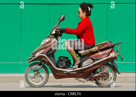 Eine chinesische Frau reist entlang einer Straße auf ihrem Roller in Kashgar. Stockfoto