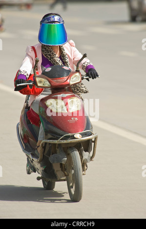 Eine chinesische Frau reist entlang einer Straße auf ihrem Roller in Kashgar eine Sonnenblende Schild tragen. Stockfoto