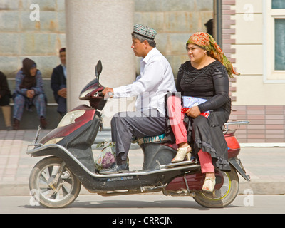 Ein paar chinesische Uygher Reisen entlang einer Straße auf ihren Roller in Kashgar. Stockfoto