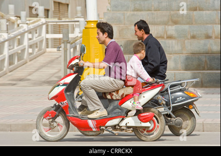 Chinesischen Vater und Sohn fahren entlang einer Straße auf ihren Roller in Kashgar. Stockfoto
