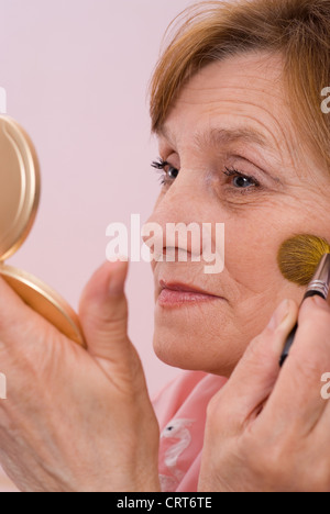 ältere Frau malt sein Gesicht und schaut in den Spiegel Stockfoto