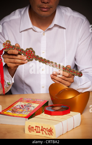 Die Hände des Mannes mit chinesischen Feng-Shui-Zubehör auf Tisch, mit einem Schwert bestehend aus Münzen Stockfoto