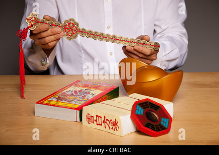 Die Hände des Mannes mit chinesischen Feng-Shui-Zubehör auf Tisch, mit einem Schwert bestehend aus Münzen Stockfoto