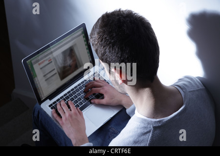Junger Mann sitzt in der Dunkelheit mit seinem Laptop auf eine generische Website. Stockfoto