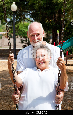 Romantische senior Mann schob seine schöne Frau in einer Schaukel auf einem Spielplatz. Stockfoto