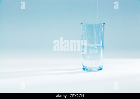 Wasser gießen in ein halb volles Glas Becher in ein blaues Licht Stockfoto