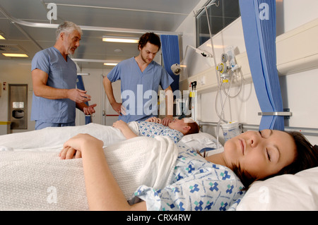 Ein Chirurg (links) und ein Mitglied von seinem chirurgischen Team sprechen mit den Patienten während der Visite im Krankenhaus. Stockfoto