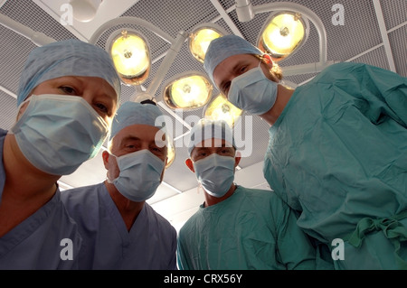 Ein Patient auf ein Team von maskierten Chirurgen unter Kunstlicht in einem Krankenhaus-OP-Saal. Stockfoto