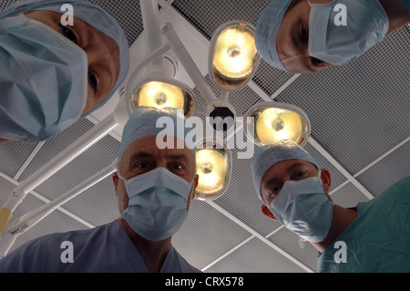 Ein Patient auf ein Team von maskierten Chirurgen unter Kunstlicht in einem Krankenhaus-OP-Saal. Stockfoto