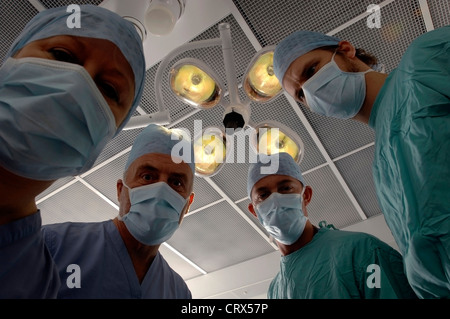 Ein Patient auf ein Team von maskierten Chirurgen unter Kunstlicht in einem Krankenhaus-OP-Saal. Stockfoto