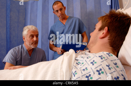 Ein bärtiger Chirurg und ein Mitglied seines chirurgischen Teams besuchen einen männlichen Patient im Bett nach einer Operation erholt. Stockfoto