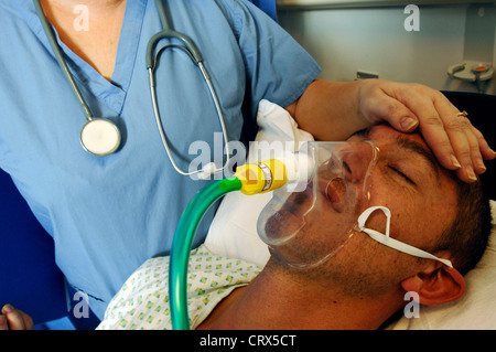 Nahaufnahme eines Mannes mit einer Sauerstoffmaske mit einer Krankenschwester Hand auf der Stirn. Stockfoto