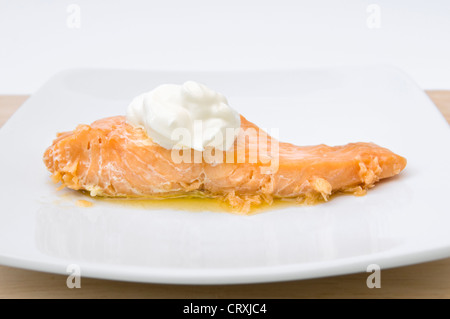 Gekochter Lachs mit Klecks Creme Fraiche und zerlassener Butter auf weißen Teller Stockfoto