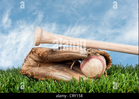 Baseball-Handschuh, Ball und Schläger Verlegung auf Rasen gegen einen blauen, leicht bewölkten Himmel für die Platzierung der Kopie. Stockfoto