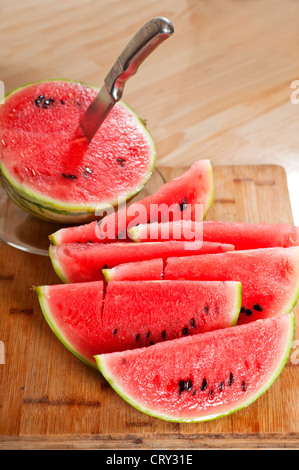 frische reife Wassermelone in Scheiben geschnitten auf einem Holztisch mit Messer Stockfoto