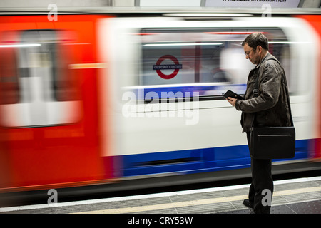 Ein Mann liest seine Kindle während des Wartens auf den nächsten Zug. Das Bild wurde aufgenommen bei Oxford Circle Stop der Londoner U-Bahn. Stockfoto