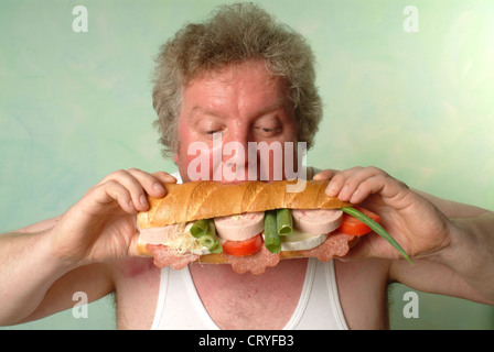 Fetter Mann im Unterhemd Essen eine große baguette Stockfoto