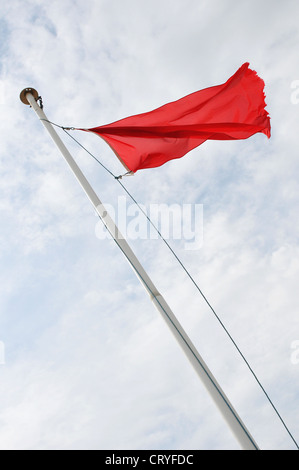 Eine rote Flagge vom Mast von unten gesehen Wolken und blauer Himmel über Stockfoto