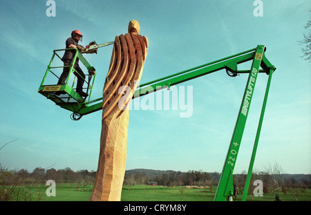 Eine Kettensäge Bildhauer auf der Plattform ein Cherrypicker schnitzen eine Gitter-Figur aus einer toten Eiche im Broadwater Park, Godalming, Surrey, England, UK. Stockfoto