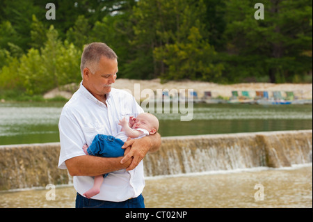 Stolzer Großvater hält sein Baby Enkel vor einem See mit dam Stockfoto