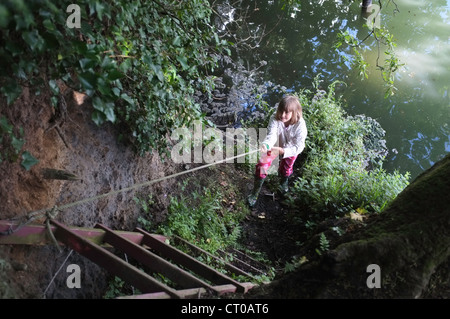 Ein neun Jahre altes Mädchen klettert ein Seil und Leiter der Penryn-Fluss in Cornwall, Großbritannien Stockfoto