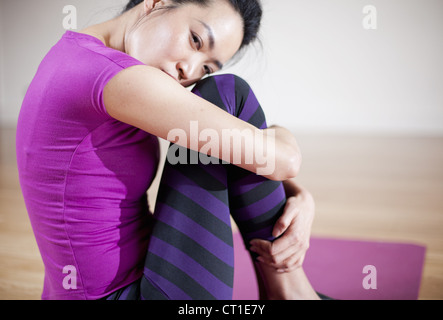 Frau umarmt ihr Knie auf Yoga-Matte Stockfoto