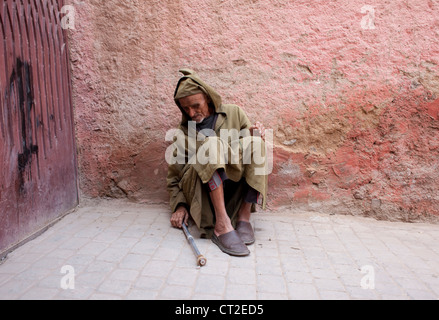 Ein älterer Mann betteln sitzt, der von einer Mauer in der Medina von Marrakesch Stockfoto